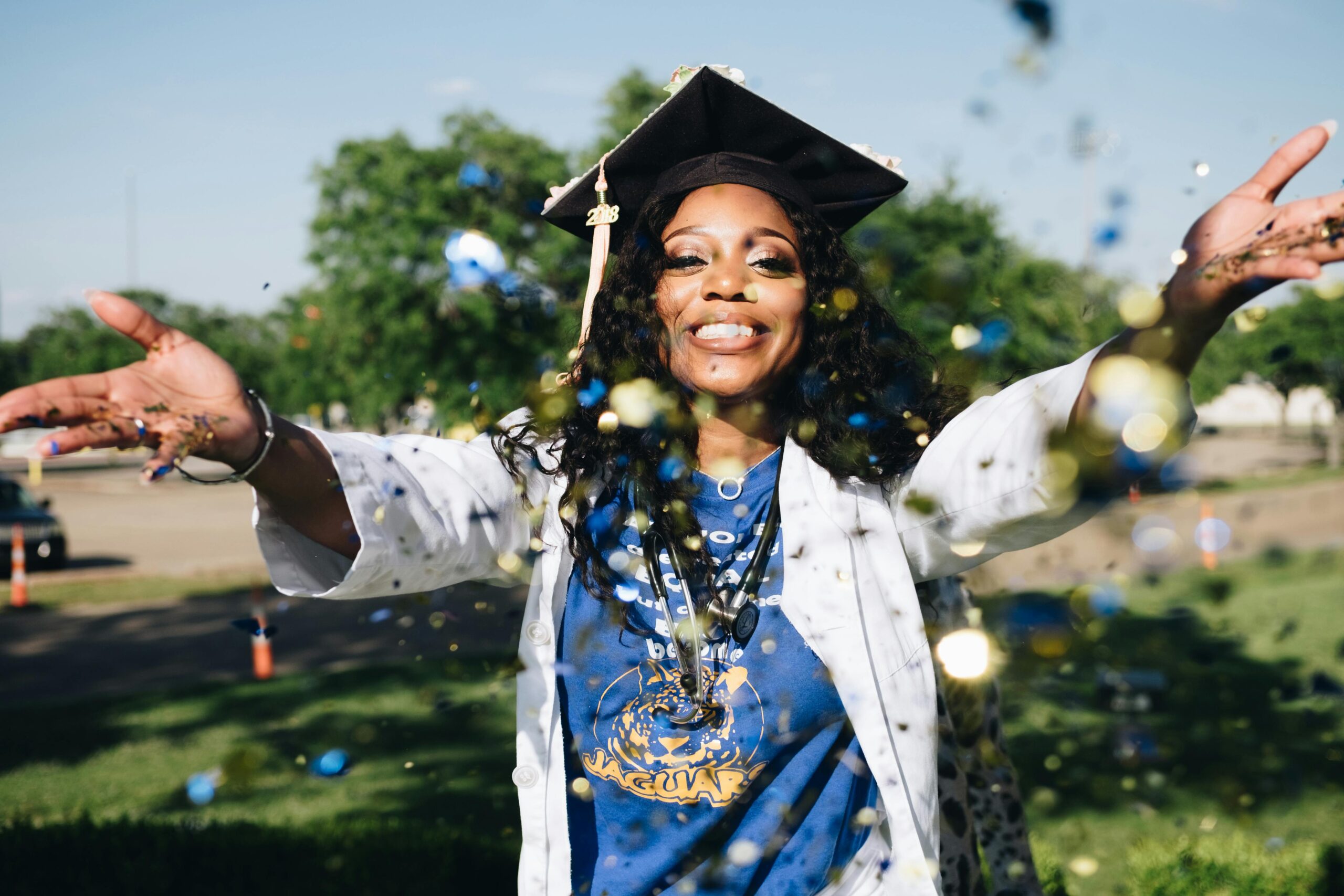 Home African American woman celebrating graduation with confetti outdoors, filled with happiness and success.